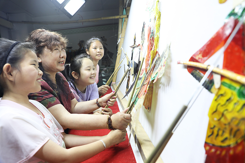 皮影藝人指導小朋友表演皮影戲。